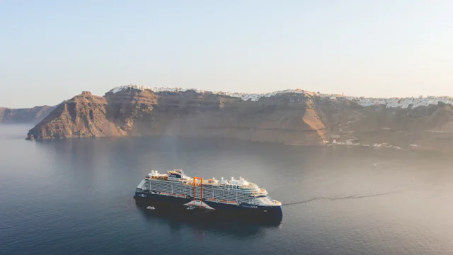 Cruiseschip vaart langs indrukwekkende kliffen en kustlijn bij een zonnige bestemming.