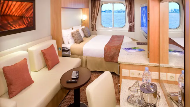 Ruime cruisehut met tweepersoonsbed, zithoek met bank en tafel, bureau met televisie en warme houten accenten in het interieur.