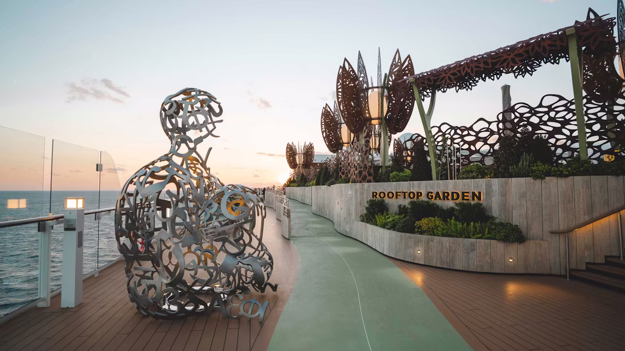 Rooftop Garden op een cruiseschip met kunstsculptuur, wandelpad en uitzicht over zee bij zonsondergang. 