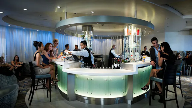 Gasten genieten van cocktails aan een bar op een cruiseschip, terwijl de bartender drankjes bereidt.