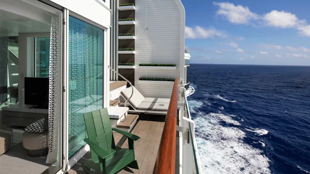 Balkon van een luxe cruisehut met zitgedeelte en ligstoel, met uitzicht over de open zee en het schip dat door het water vaart