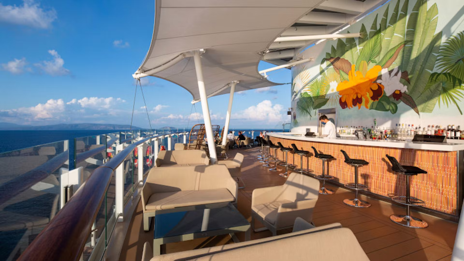 Buitenbar op het dek van een luxe cruiseschip met zitplekken, uitzicht op zee en een zonnige, tropische sfeer