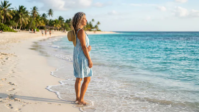 Vrouw geniet in haar eentje van een rustige wandeling langs een wit tropisch strand met turquoise water en palmbomen in het Caribisch gebied.